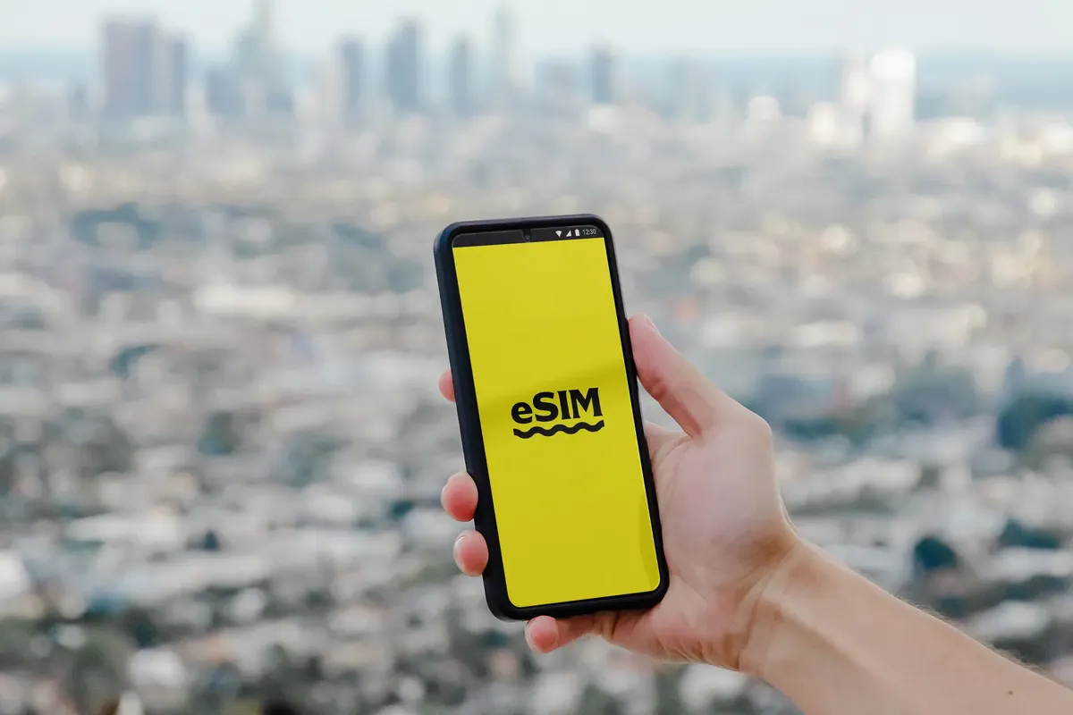 Hand holding a smartphone showcasing eSIM technology with a blurred Los Angeles skyline in the background.
