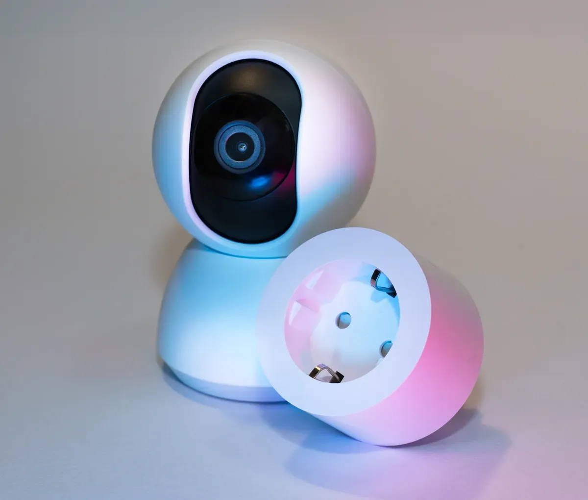 Smart home security camera and plug socket on a neutral background.